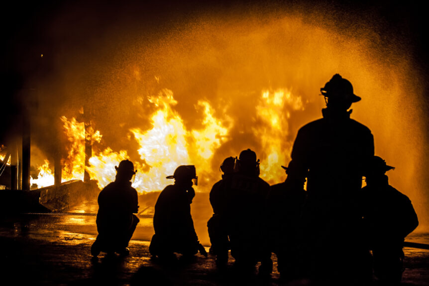 firefighters stand in front of an out-of-control blaze