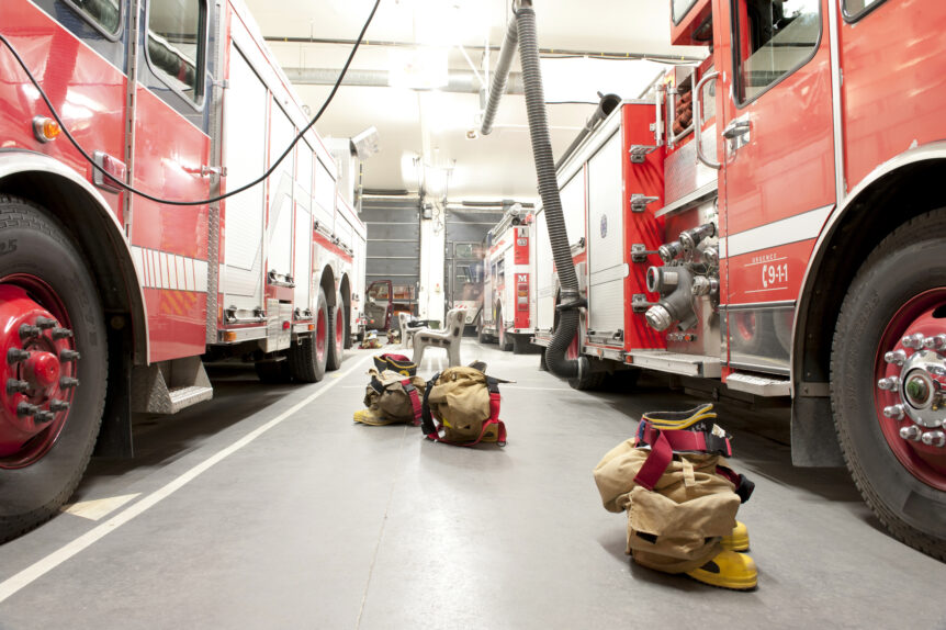 Firefighter gear sits on the ground between two fire apparatuses in a fire station